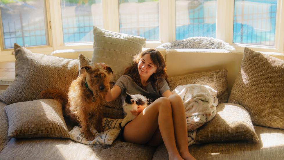 why pets need year-round heartworm prevention; woman sits on couch with dog and cat